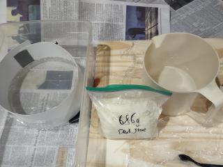 A bag of dental stone next to a plastic jug and a mirror with shiny cardstock taped along its edge forming a lip
